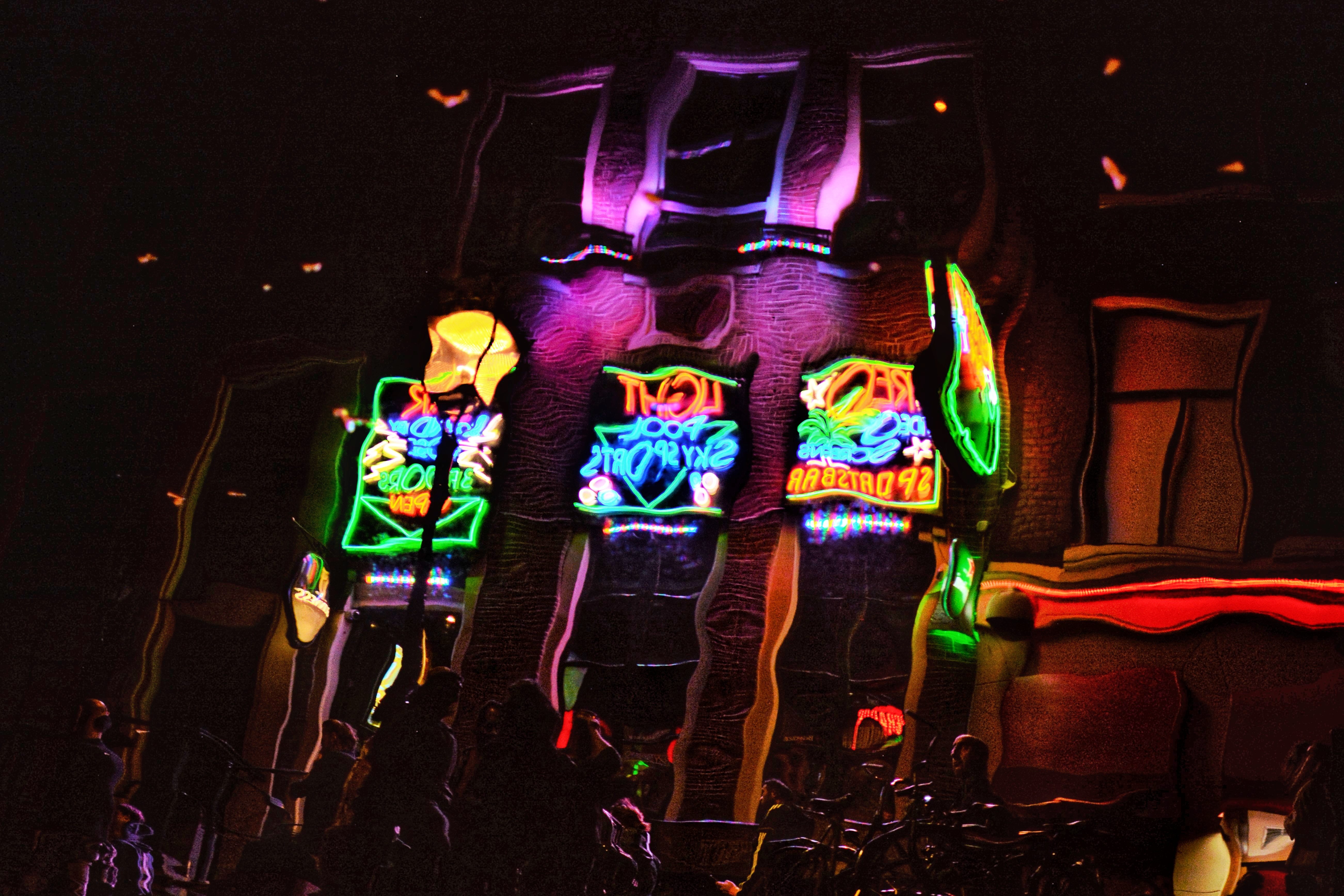 A photograph of a few storefronts and their neon signs in Amsterdam at night. The photograph is flipped horizontally so the store signs are unreadable, and a wave filter is applied, making the buildings look squiggly.