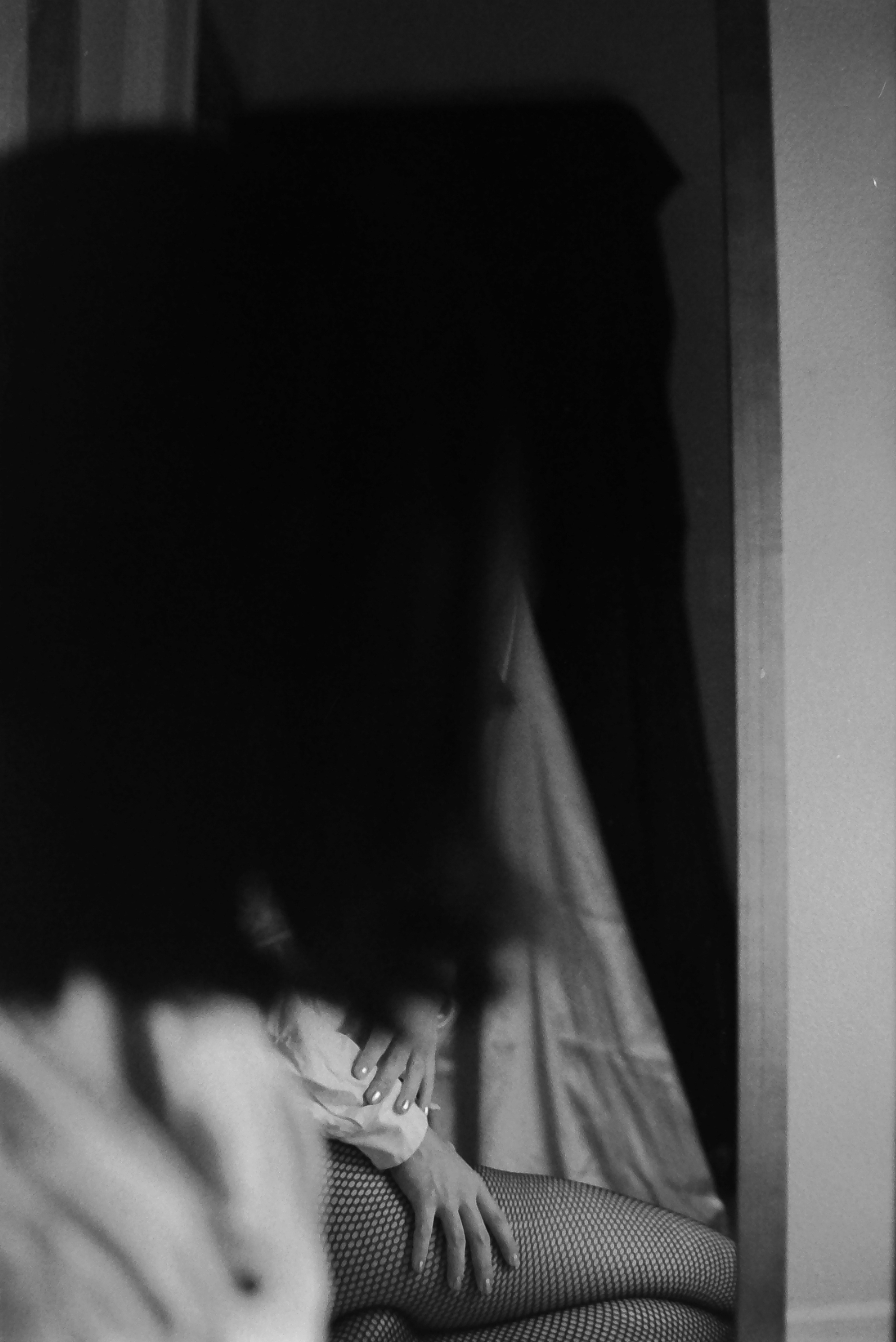 A blurred person's profile hides the body of the woman in the mirror. One can see that woman's hands and fishnet stockings in this monochromatic photograph.