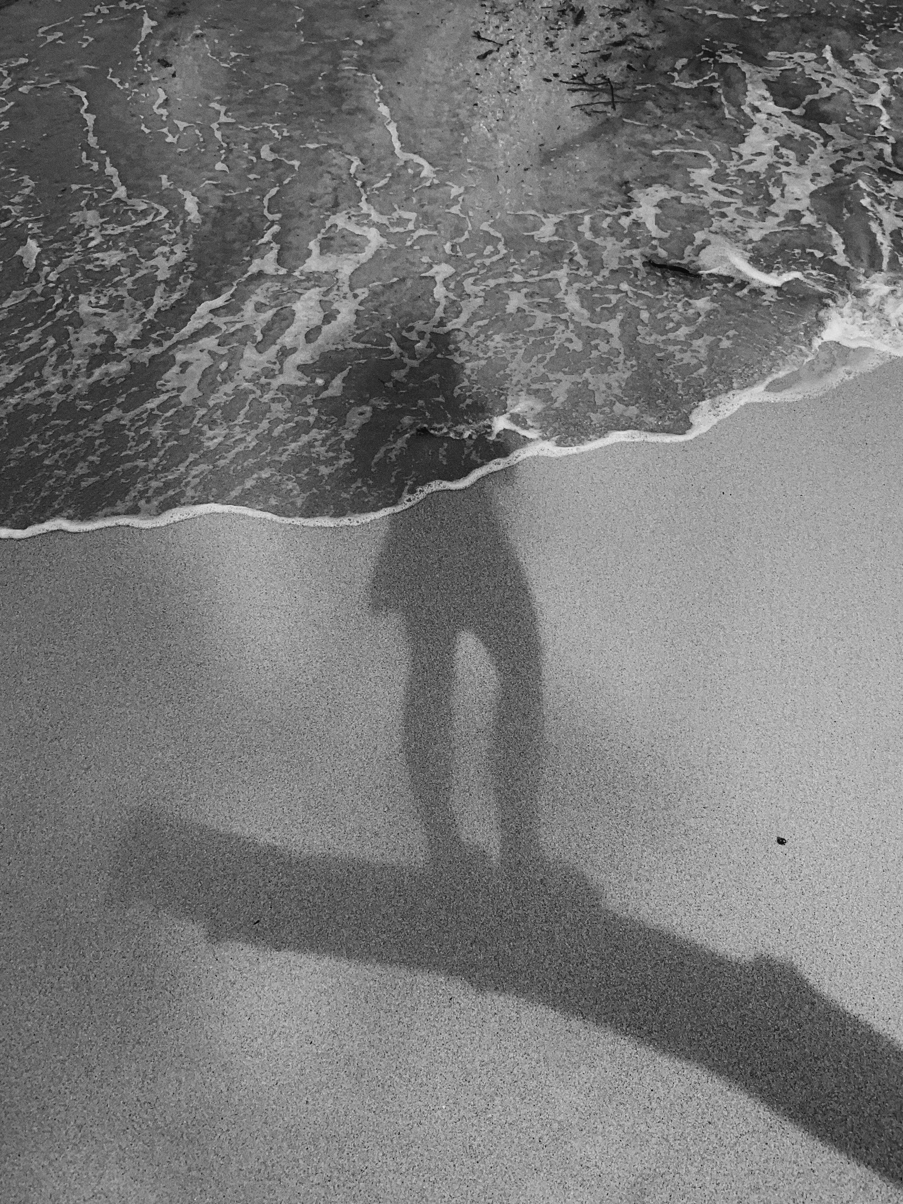 Medium: Photography. Shown is the shadow of a girl standing on a branch at the shore of a beach.