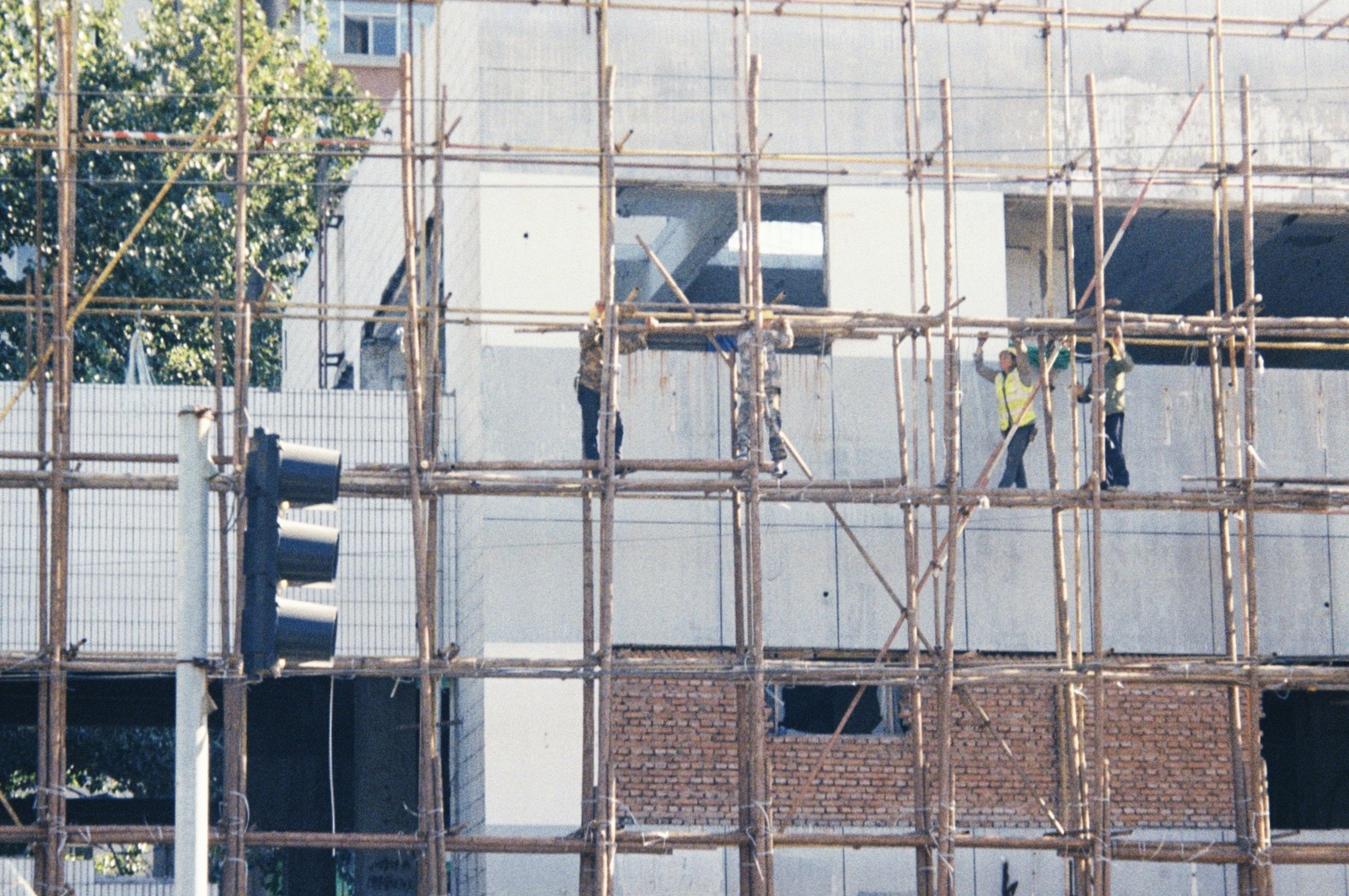 A slightly grainy photograph of four construction workers building scaffolding. In the background is a cement and brick building.